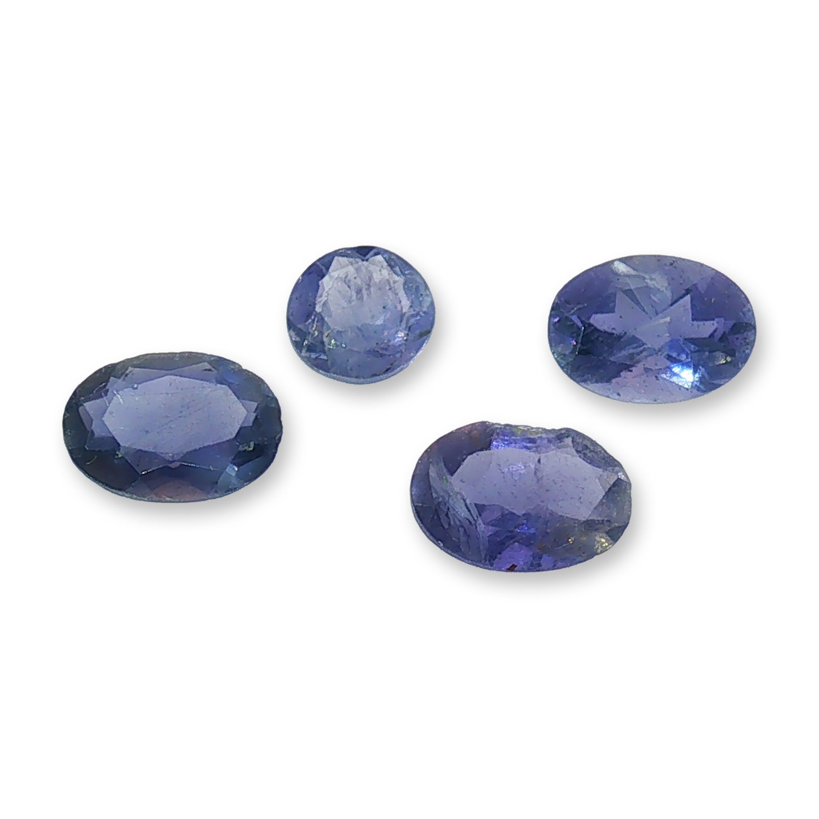 Set of Four Loose Faceted Iolite Gemstones: Collection of four loose faceted gemstones, appearing to be iolite, displaying a deep purplish-blue hue. The set includes a mix of faceted oval and round cuts, providing varied options for jewelry