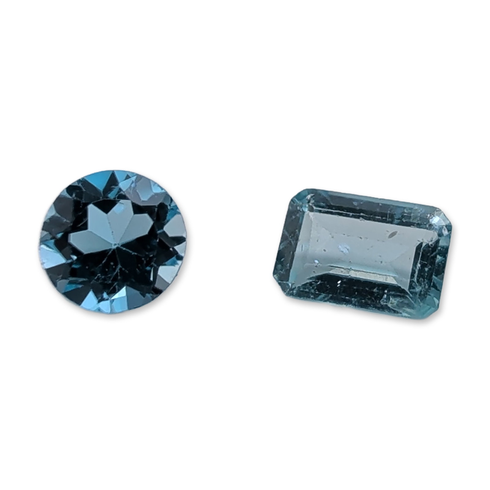 Two Loose Faceted Blue Gemstones: Two loose faceted gemstones in varied shades of blue. The first is a round brilliant-cut stone with a saturated, vibrant medium-to-dark blue tone, resembling Swiss blue topaz. The stone displays eye-c