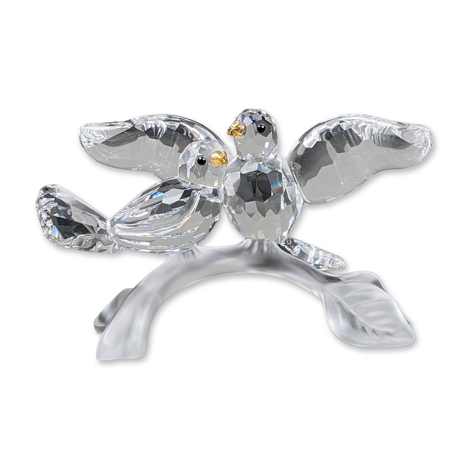 Swarovski Crystal Figurine, Turtledoves: Two faceted clear crystal birds, part of the Feathered Beauties Collection, with amber-toned crystal beaks and black eyes perched on a frosted crystal branch base with a single leaf. One bird is depic