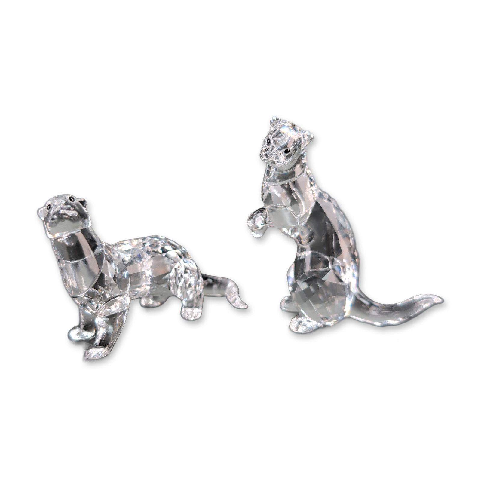 Swarovski Crystal Otters Pair Figurines: Swarovski pair of otters in faceted clear lead crystal, one depicted in a prowling stance and the second in a seated position. Each piece features precision-cut facets throughout the body. Each figuri