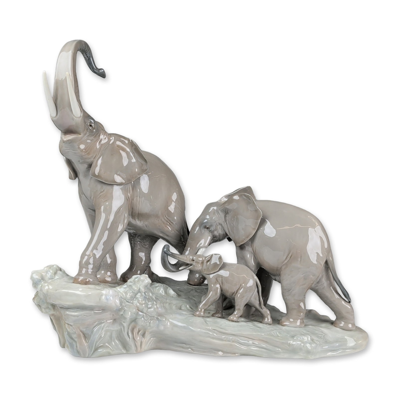 Lladro Porcelain Figurine, Elephants 01001150: Sculpted by Fulgencio Garcia. The composition depicts a family of three elephants traversing a rocky, textured landscape, including a large bull with a raised trunk and tusks, an adult cow, and a youn
