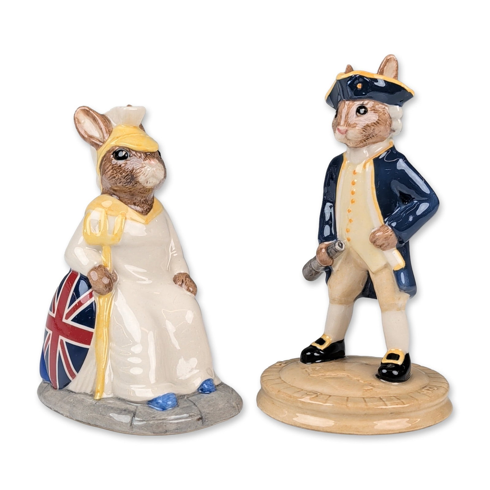 Pair of Royal Doulton Bunnykins Figurines: Royal Doulton. Pair of Bunnykins figurines in glazed ceramic, featuring Captain Cook and Britannia. Captain Cook (DB 251) depicts a rabbit in 18th-century naval attire with a navy blue coat and tricor