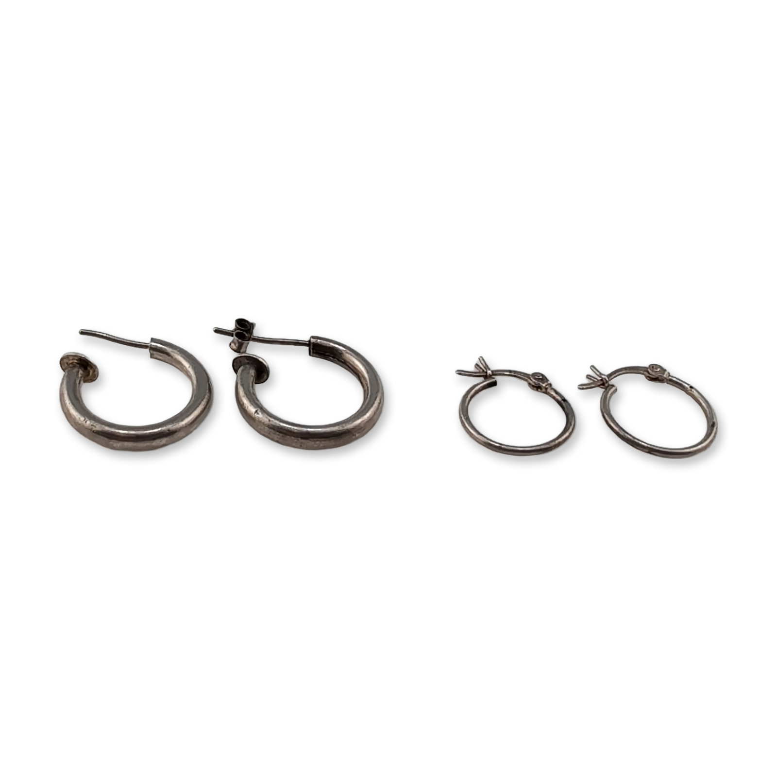Two Pairs of Sterling Silver Hoop Earrings: Two pairs of contemporary sterling silver hoop earrings. The first pair consists of small, thin circular hoops with hinged wire and U-catch closures. The second pair features thick, tubular open
