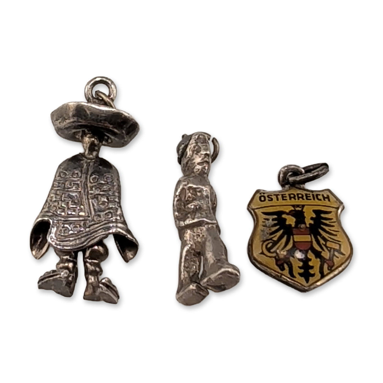 Trio of Vintage Silver Souvenir Charms: The lot features an enameled shield charm depicting the Austrian coat of arms on a yellow field, inscribed OSTERREICH along the edge. The reverse displays an AW and 800 silver mark. A second small cas