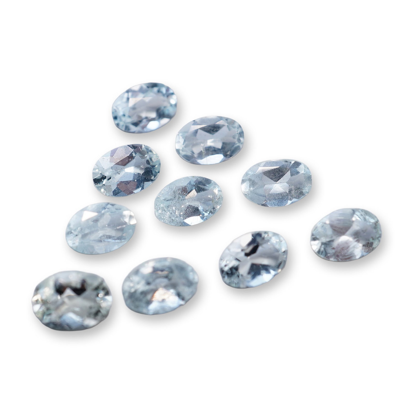 Group of Ten Oval Faceted Aquamarine Loose Gemstones: Group of ten loose gemstones in aquamarine, featuring an oval faceted cut. The stones exhibit a uniform pale blue hue with characteristic watery transparency. Multiple stones show visible internal inc