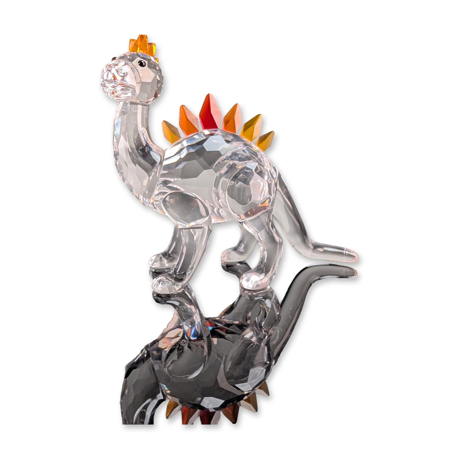 Swarovski Crystal Dino Stegosaurus Figurine: Swarovski Dino the Stegosaurus figurine in faceted clear lead crystal. The stylized figure features a clear faceted body with seven upright dorsal plates in a yellow, amber, and red color gradient. Th