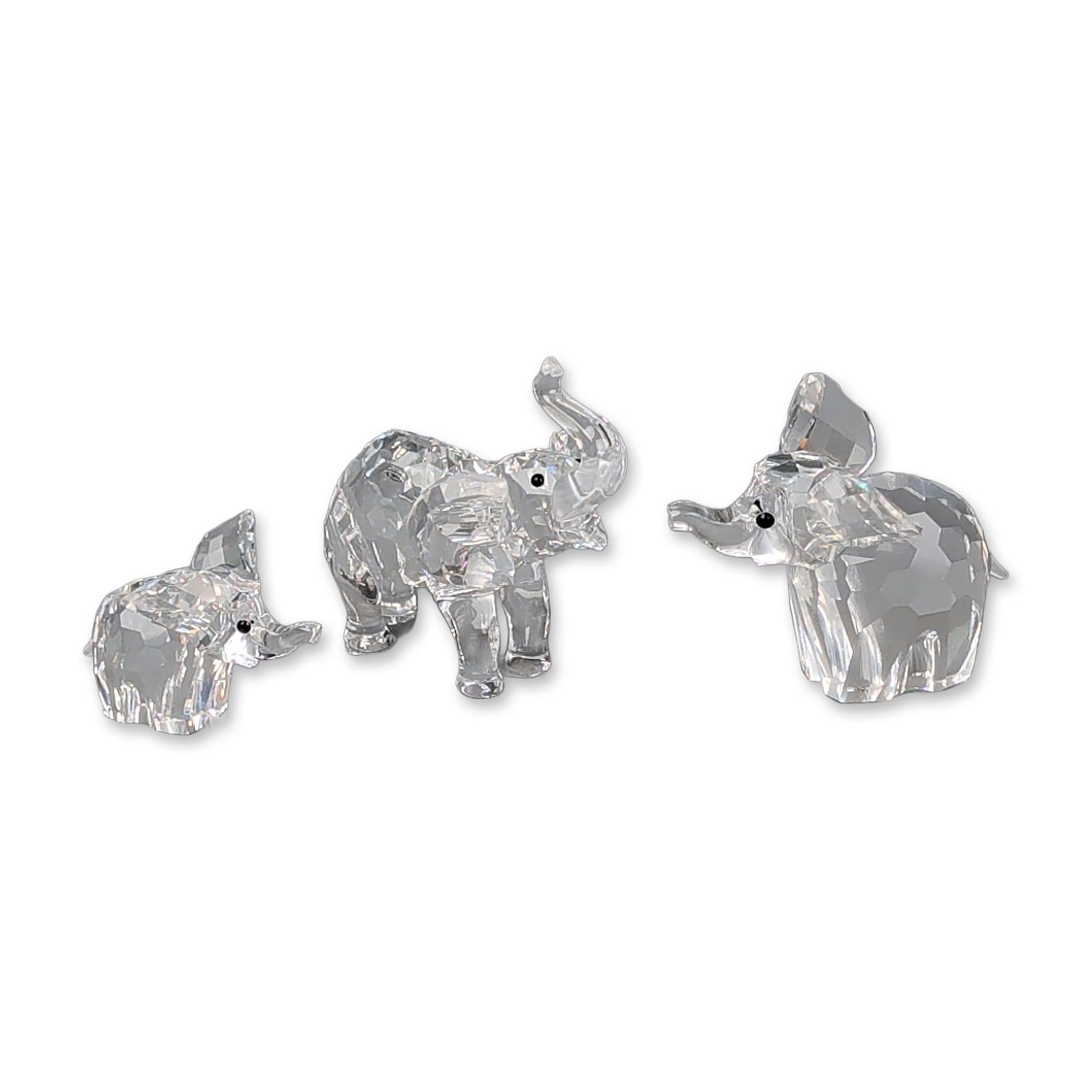 Three Swarovski Silver Crystal Figurines, Elephants: Swarovski. Trio of elephant figurines in faceted clear lead crystal, each with inset black bead eyes. The set includes a large elephant with its trunk curved downward toward the chest, a medium-sized 