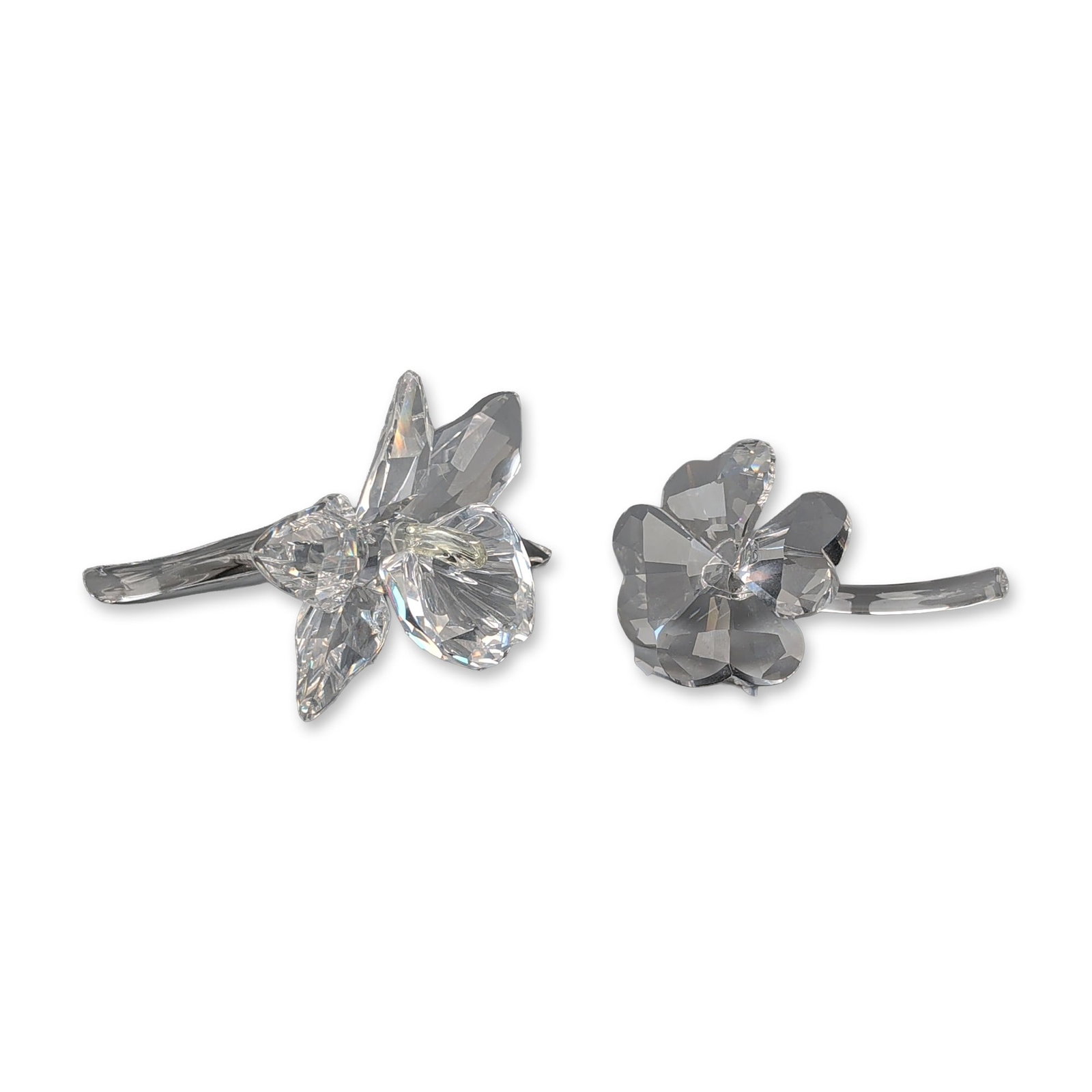 Two Swarovski Silver Crystal Figurine, Orchid and Clover: Swarovski Silver Crystal. Two floral figurines in faceted clear lead crystal. One figurine depicts an orchid with multiple faceted petals and a pale yellow tinted central element, mounted on a curved 