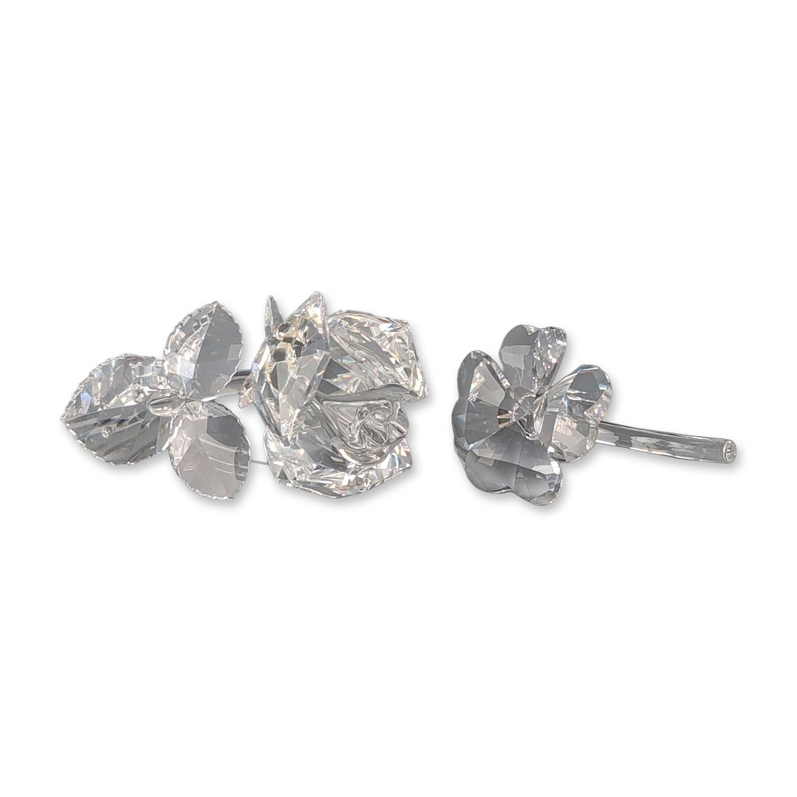 Two Swarovski Silver Crystal Rose and Four-Leaf Clover Figurines: Two figurines in faceted clear lead crystal, featuring a long-stemmed rose with three leaves and a four-leaf clover on a curved stem. Both pieces are accompanied by original grey cylindrical cardboard