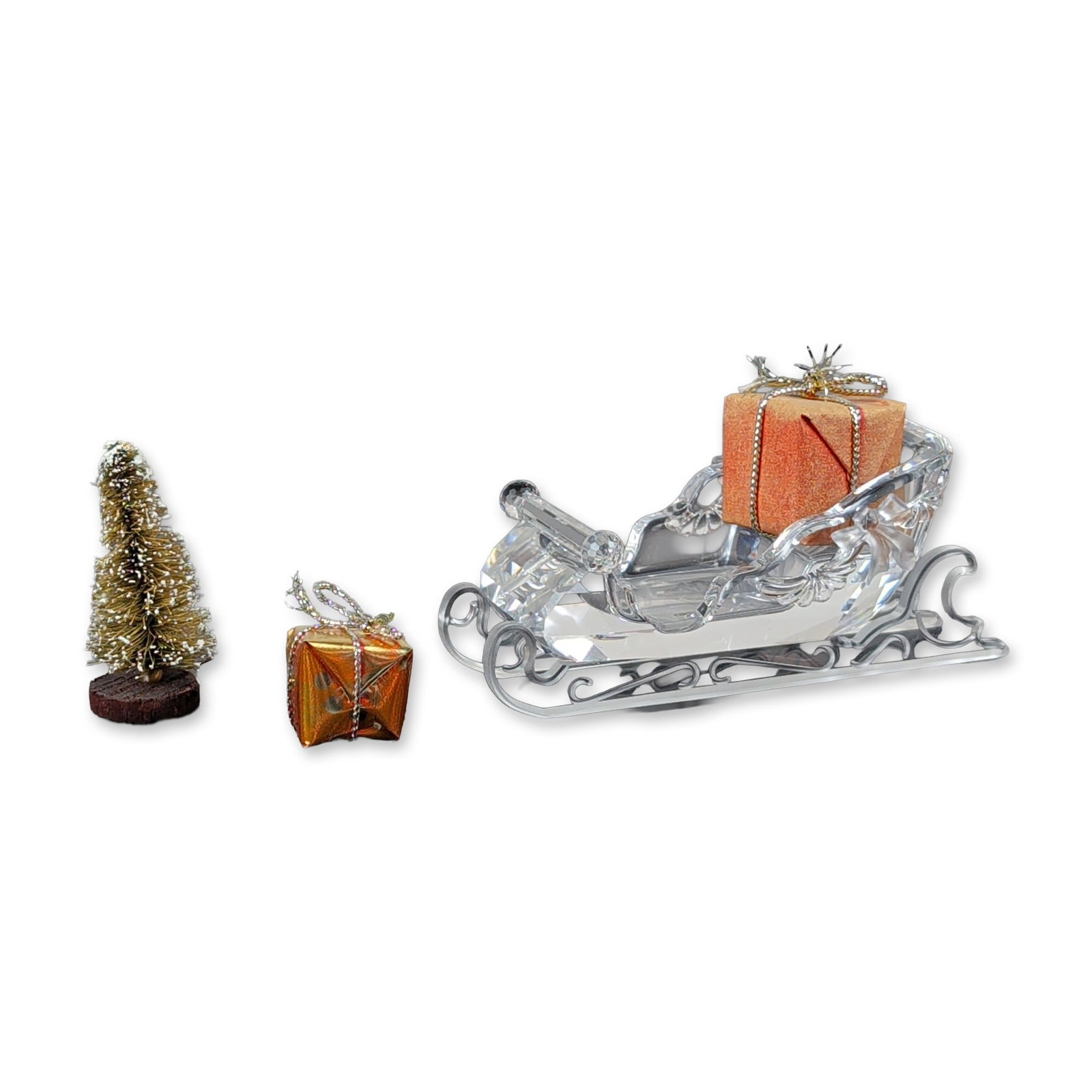 Swarovski Silver Crystal Christmas Sleigh Set: Swarovski Silver Crystal Santa's sleigh set in faceted lead crystal, featuring an ornate sleigh with scrollwork runners. The set is accompanied by two miniature gift-wrapped parcels, one in a textured