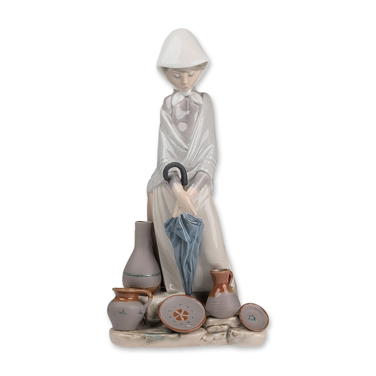 Lladro Porcelain Figurine, Ceramic Seller Woman 01005081: Lladro, Spain. Glazed porcelain figurine sculpted by Juan Huerta. The figure is depicted in traditional attire including a white pointed bonnet, grey fringed shawl, and tan skirt, holding a furled blu