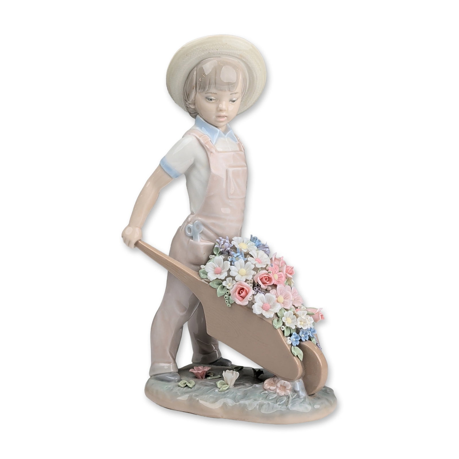 Lladro Porcelain Figurine, Little Gardener 01001283: Lladro glazed porcelain figurine designed by Francisco Catala. The piece depicts a young boy wearing a wide-brimmed straw hat and overalls with blue trim, pushing a wheelbarrow filled with an assortme