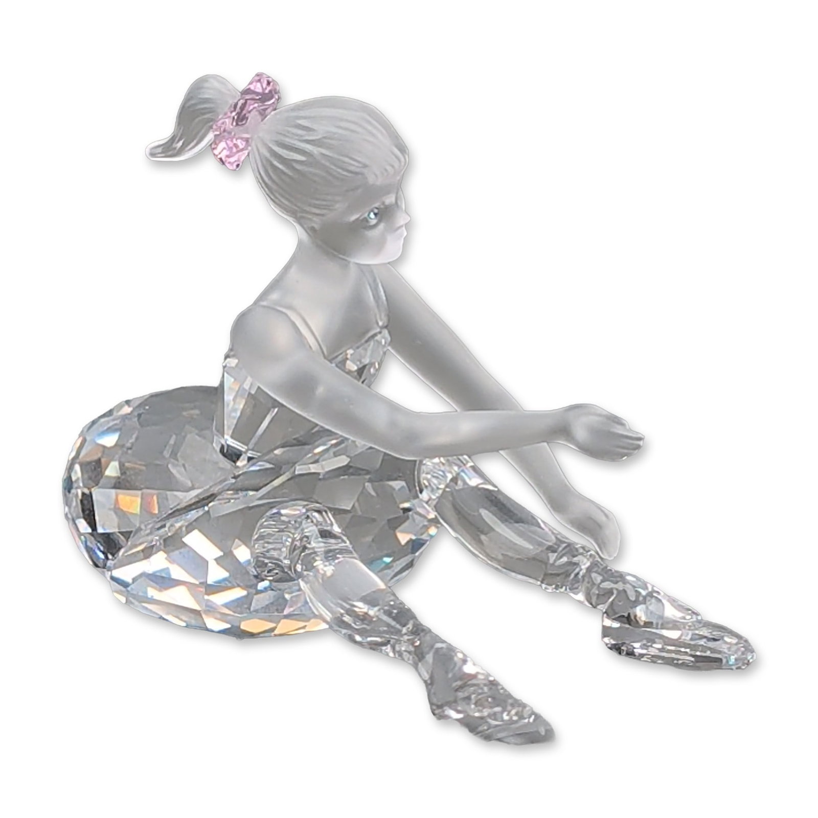 Swarovski Crystal Figurine, Young Ballerina: Sitting figurine in frosted and faceted lead crystal. The design features a frosted crystal head, torso, and arms, detailed with blue crystal eyes and a faceted pink crystal hair accessory in the pony