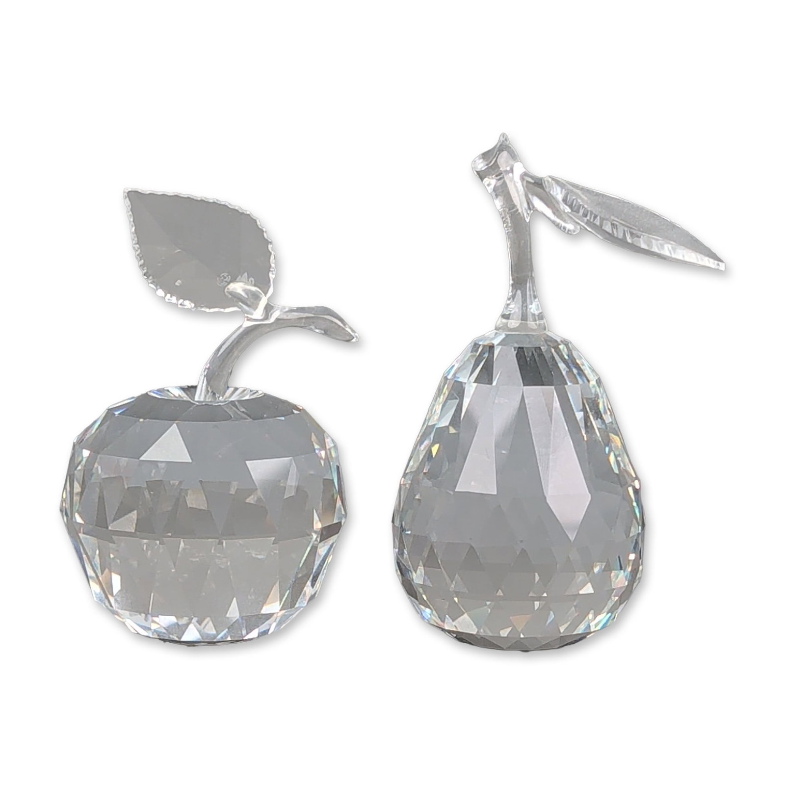 Two Swarovski Silver Crystal Apple and Pear Figurines: A pair of faceted lead crystal fruit figurines featuring an apple and a pear. The apple figurine consists of a faceted clear crystal body, a smooth curved crystal stem, and a single frosted crystal le