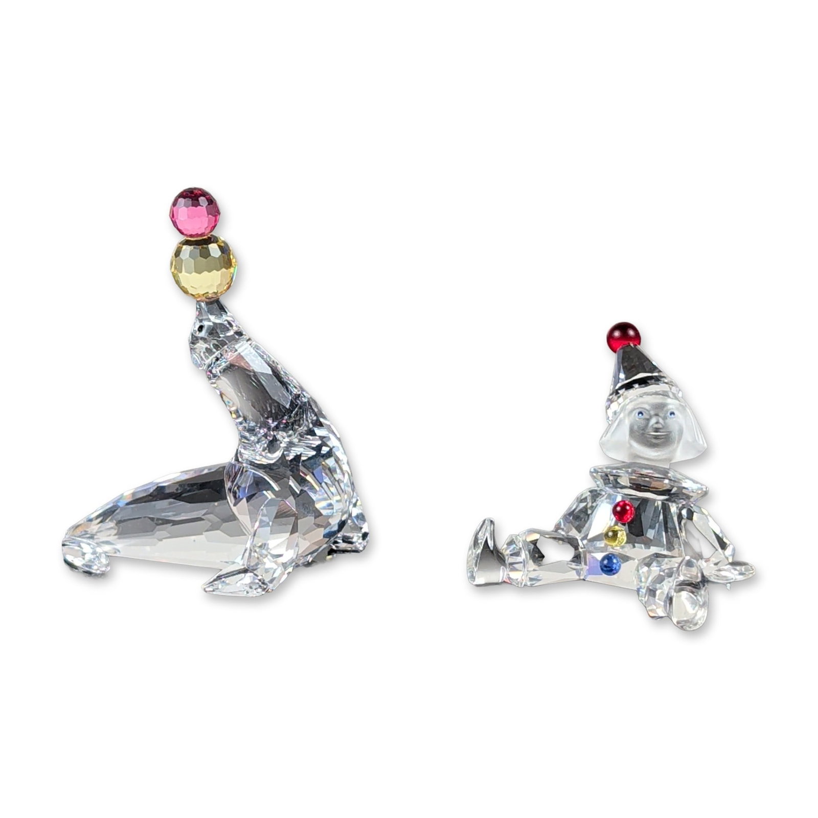 2pc Swarovski Crystal Puppet and Seal Figurines: Swarovski crystal figurines featuring a puppet clown and an seal. Faceted lead crystal construction with frosted and colored crystal accents. The standing clown includes a frosted face, red nose, and