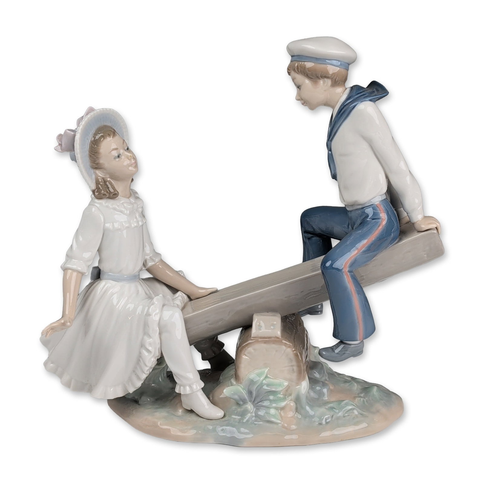 Lladro Porcelain Figurine, See-saw 01001255: The composition features a young boy in a sailor uniform and a girl in a ruffled white dress with a matching bonnet, playing on a seesaw fashioned from a log. The figures are finished in a traditional