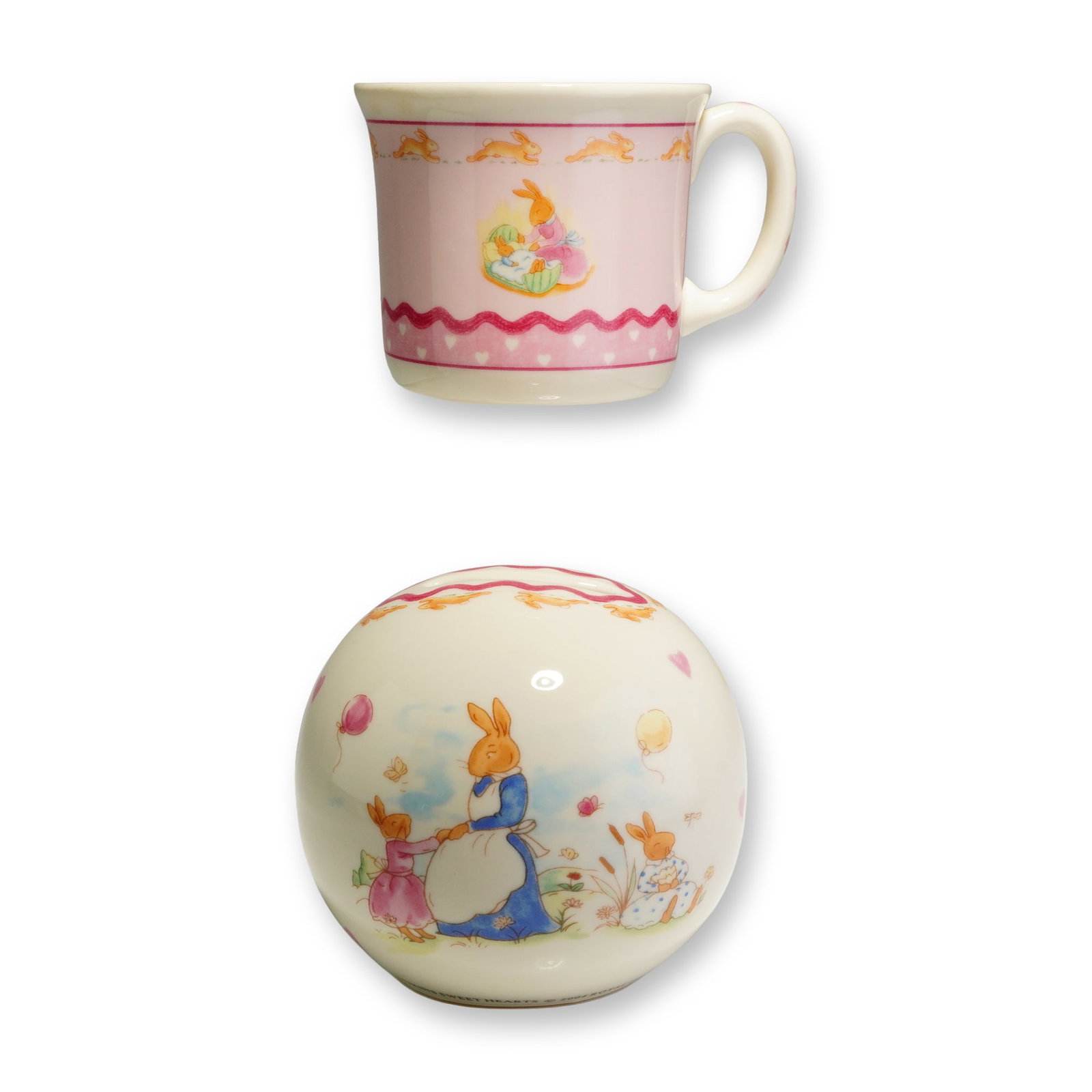 2pc Royal Doulton Bunnykins Sweet Hearts Mug and Money Bank: The handled mug and spherical money box are crafted from bone china with a cream-colored ground, while the mug features a prominent pink area as its main background. Both pieces showcase colorful illu