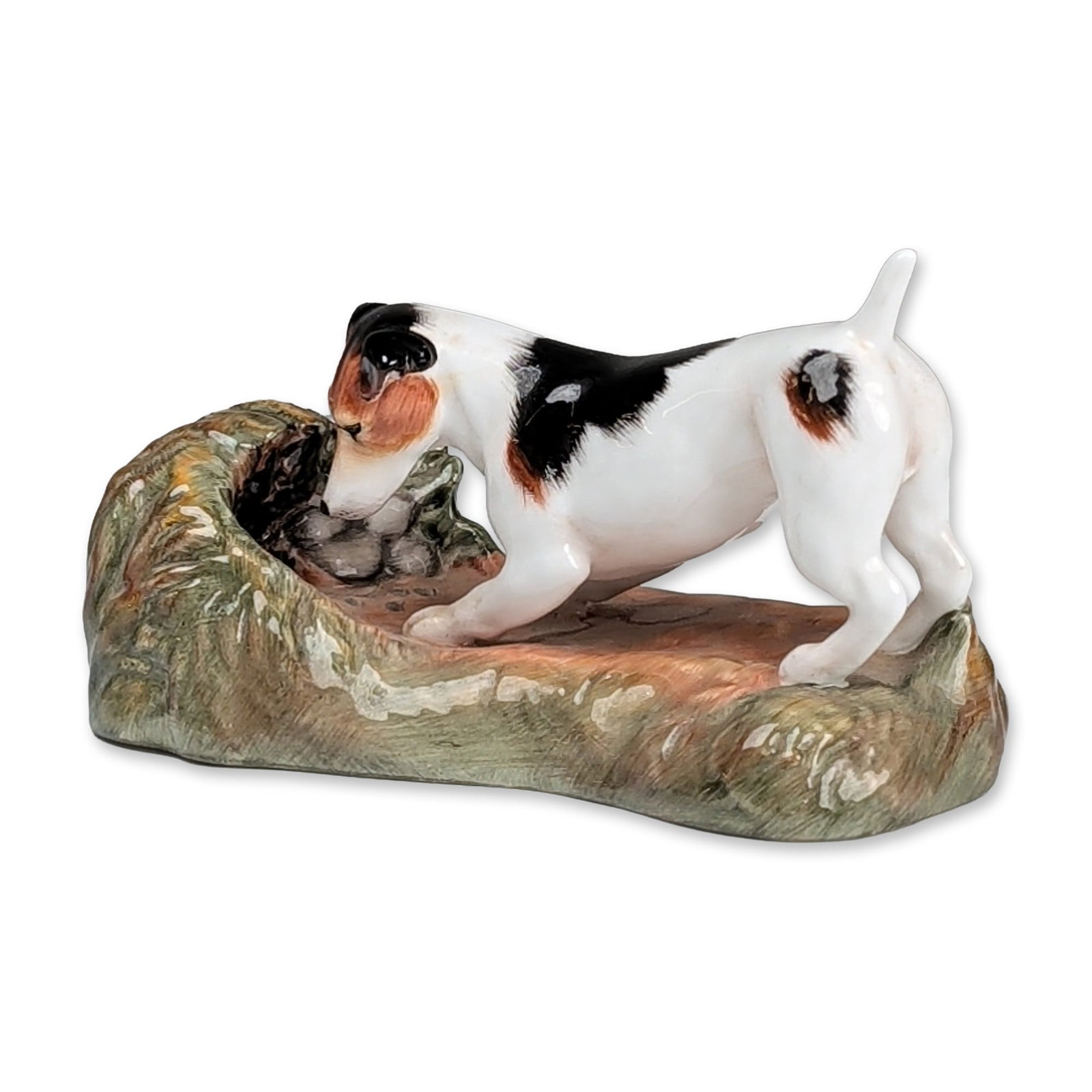 Royale Stratford Dog Figurine, Jack Russell Terrier: The piece depicts a smooth-coated terrier in an active hunting pose investigating a hollowed log or burrow. The dog is rendered with a white coat featuring black and tan markings, while the naturalist