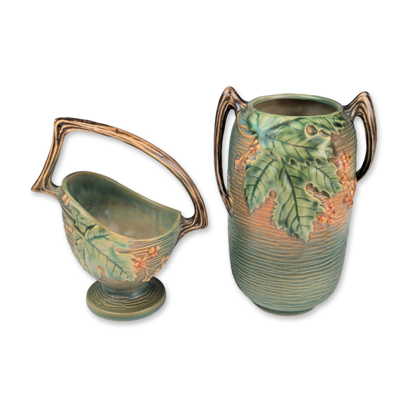 Roseville Art Pottery Vase and Basket Cachepot, Green Bushberry: A pair of art pottery vessels in the Bushberry pattern, introduced in 1941, featuring relief-molded green leaves and orange-toned berries against a vertically ribbed textured ground. The two-handled v