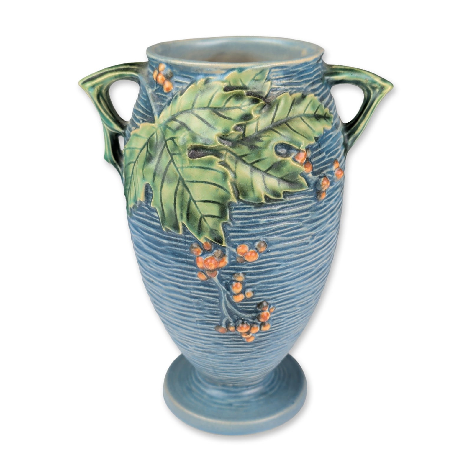 Roseville Pottery Two Handled Vase, Blue Bushberry: Two-handled earthenware vase in the Bushberry pattern with a matte blue glaze, featuring a horizontally ribbed texture and relief-molded decoration of serrated green leaves and orange berry clusters. 