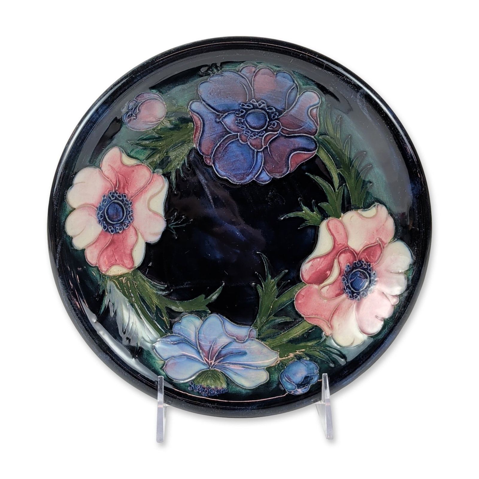 Walter Moorcroft Anemone Pattern Ceramic Plate: Walter Moorcroft (British, 1917-2002). Shallow display plate in tube-lined earthenware, featuring the Anemone pattern with floral motifs in shades of pink, purple, and blue glazes set against a deep c