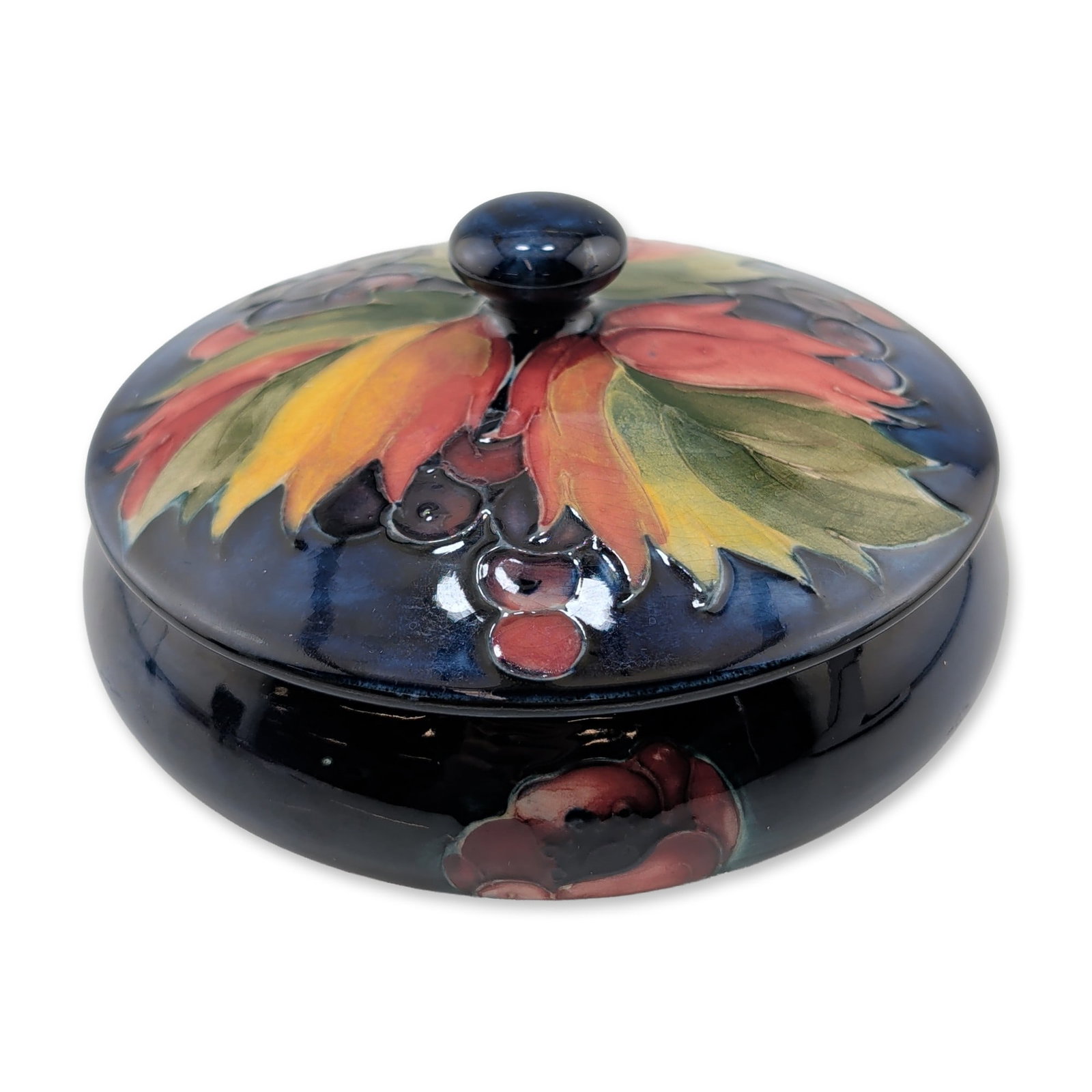 Moorcroft Pottery Leaf and Berry Lidded Dish: Moorcroft, England, circa 1930-1940s. A circular lidded candy dish in glazed earthenware featuring the Leaf and Berry pattern designed by William Moorcroft. The exterior of the lid is decorated with t