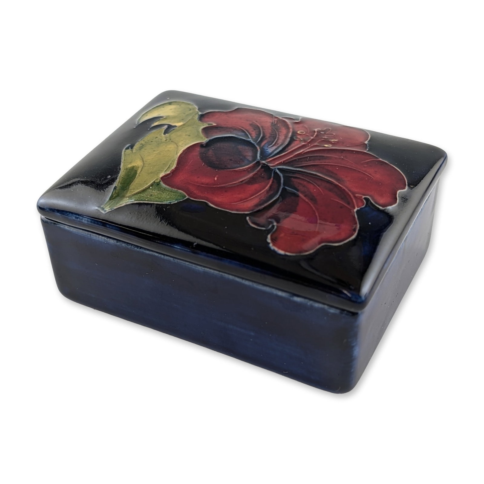 Moorcroft Pottery Hibiscus Pattern Lidded Box: Moorcroft, England, circa 1970s. Rectangular lidded trinket box in earthenware, featuring the Hibiscus pattern designed by Walter Moorcroft. The hand-painted decoration utilizes tube-lining to define 