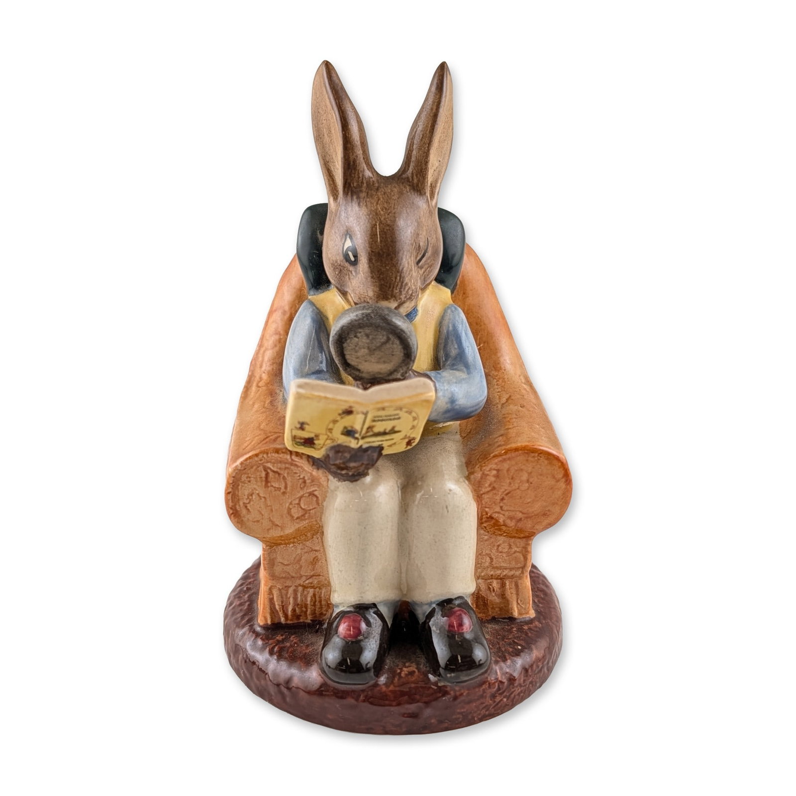 Royal Doulton "Collector Bunnykins" Ceramic Figurine: Royal Doulton "Collector Bunnykins" figurine, model DB 54, in glazed ceramic. Modeled by Diane Lyttleton, the figure depicts an anthropomorphic rabbit seated in a tufted orange armchair, wearing a yel