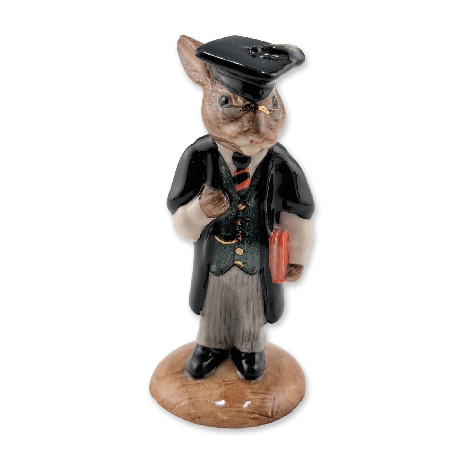 Royal Doulton Schoolmaster Bunnykins Ceramic Figurine: Royal Doulton Schoolmaster Bunnykins, model DB 60. A glazed ceramic figurine depicting a rabbit in academic attire, including a black mortarboard cap, spectacles, and graduation gown over a green wais