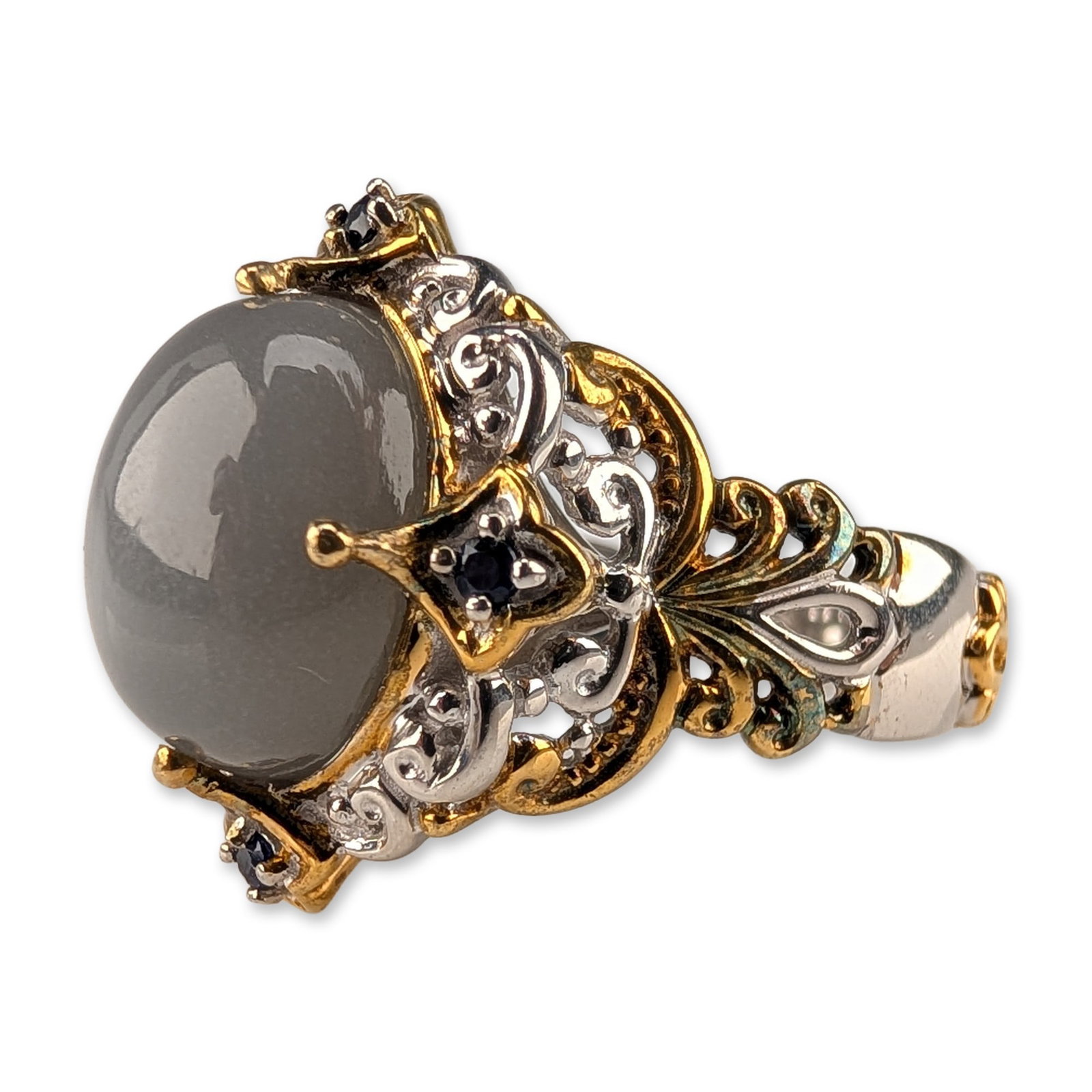 Michael Valitutti Sterling Silver Grey Moonstone and Sapphire Cocktail Ring: Ornate cocktail ring in sterling silver with yellow gold plated accents, featuring a large oval grey moonstone cabochon center stone. The elaborate two-tone setting is composed of intricate openwork f