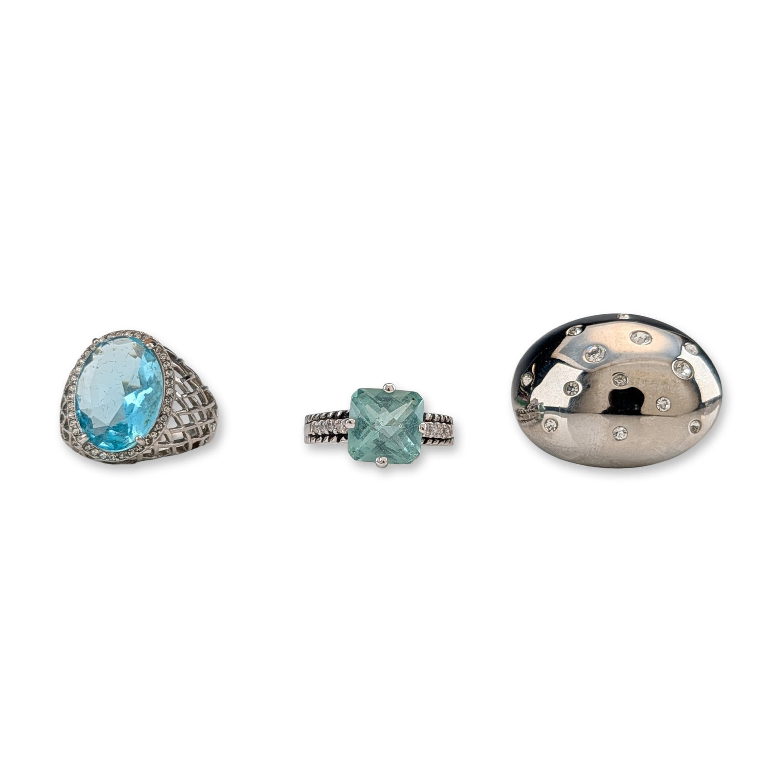 3pc Stainless Steel and Silver-Tone Cocktail Rings: A trio of cocktail rings featuring assorted faceted stones and clear accents. The collection includes a ring set with a faceted oval light blue stone held by prongs within a halo of clear stones and a
