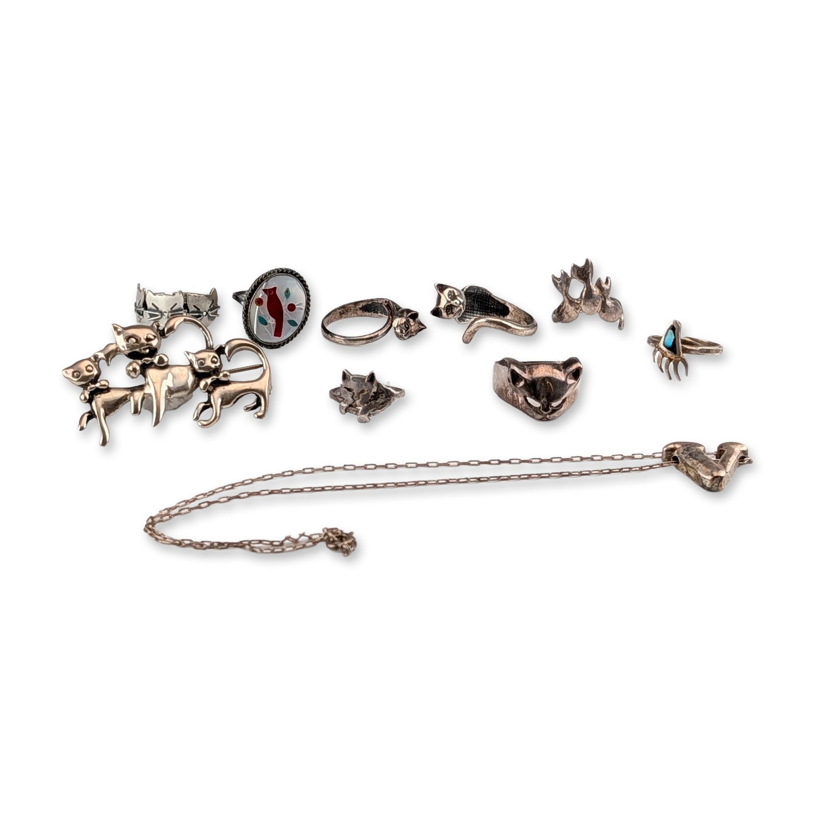 10pc Sterling Silver Cat and Animal Jewelry Collection: A collection of sterling silver jewelry featuring various feline and animal motifs. The grouping includes a large figural brooch depicting three stylized cats, six rings with cat designs, and a neckla