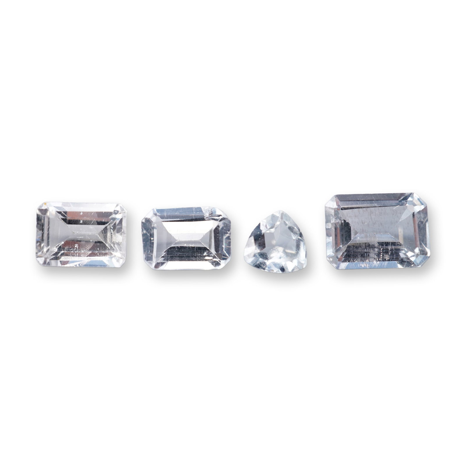 Group of Loose Aquamarine Gemstones: Group of loose aquamarine gemstones, comprising three emerald cut examples and one trillion cut example. The stones are near-colorless and transparent. Visual inspection reveals various internal