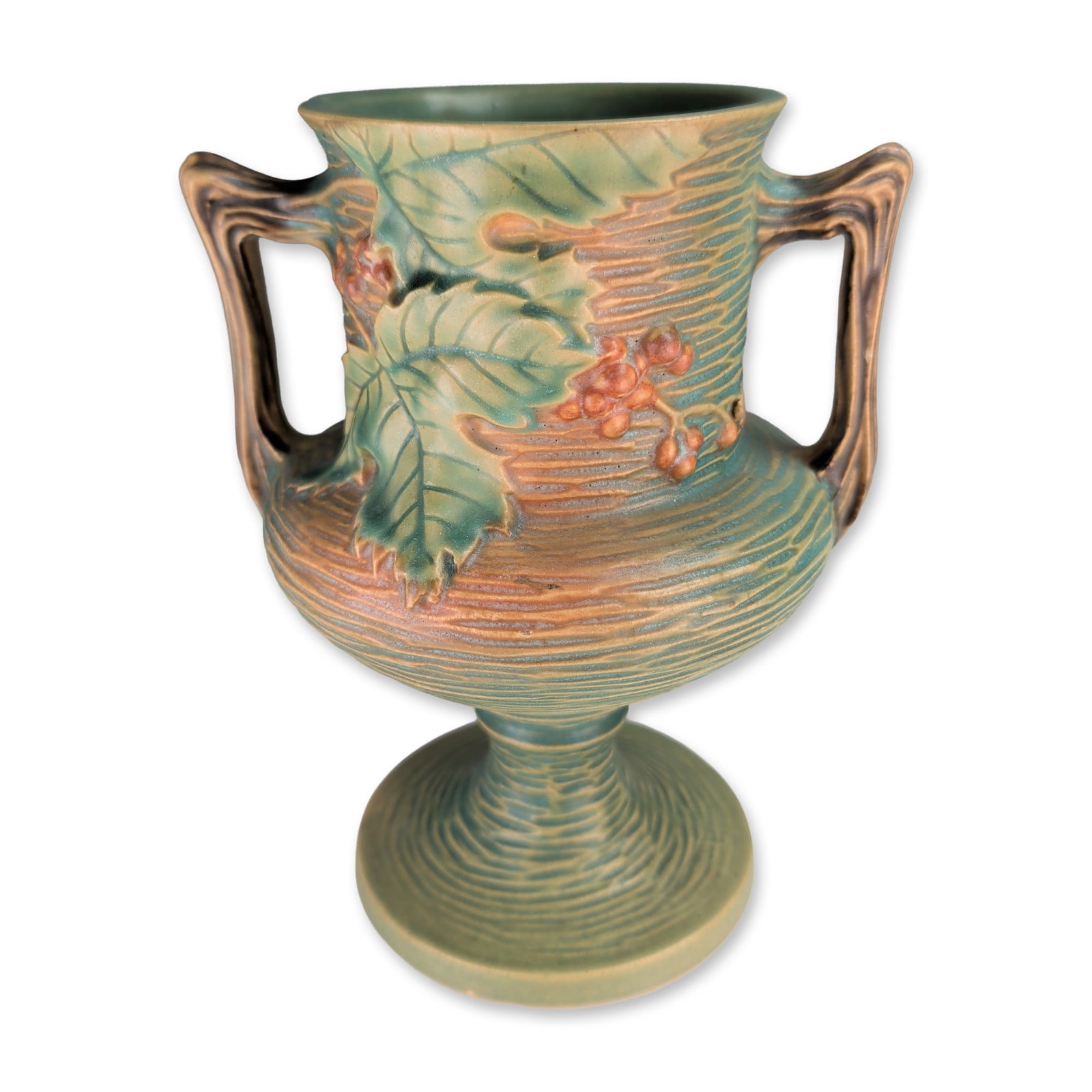 Roseville Pottery Green Bushberry Pedestal Vase: Roseville Pottery pedestal vase in the Bushberry pattern, featuring two handles and relief-molded serrated leaves with orange-red berries against a textured green and russet brown bark-like ground. Th