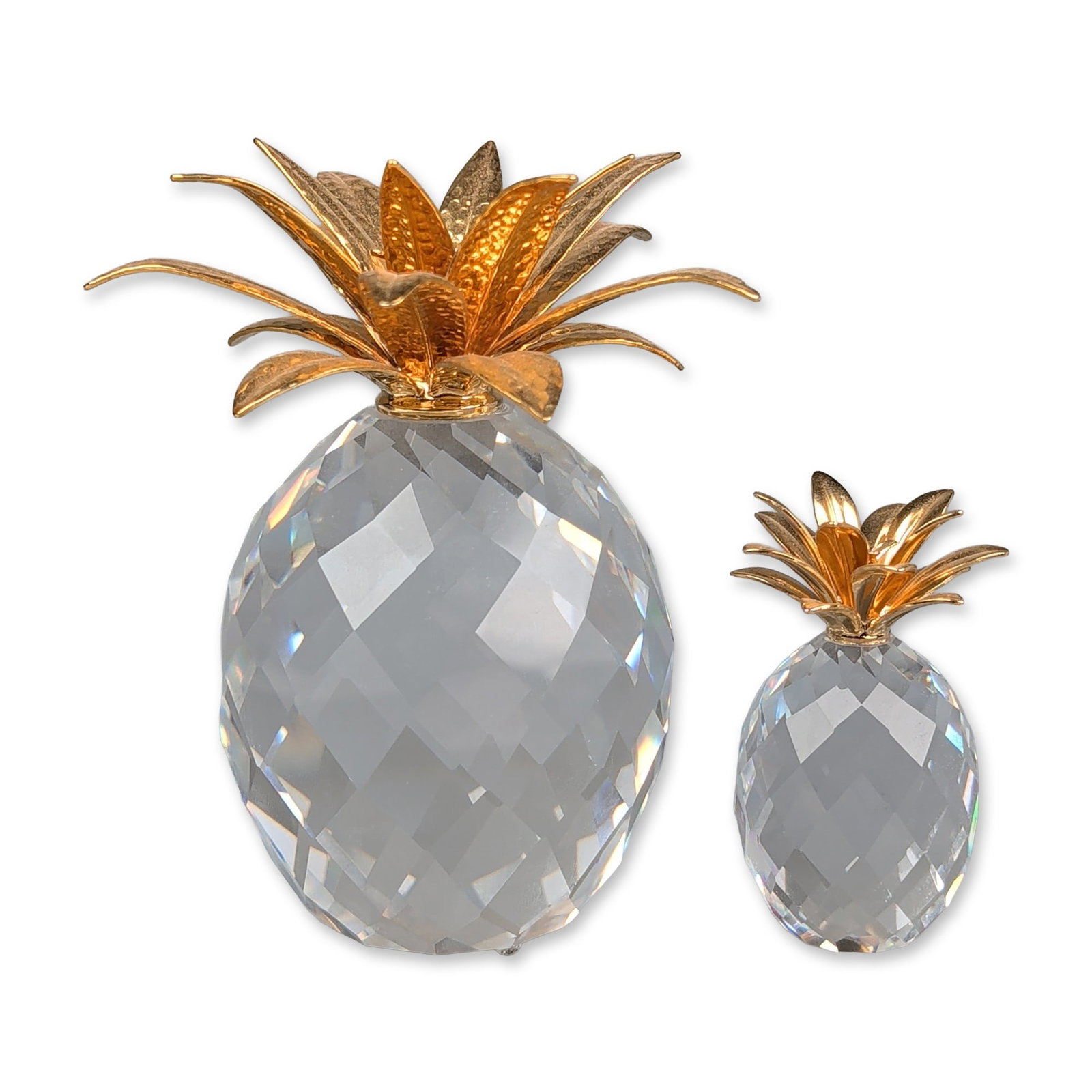 Two Swarovski Crystal Pineapple Figurines, Gold and Hammered Gold: Swarovski faceted clear crystal pineapple figurines with gold-plated foliate crowns. One larger figure features multi-tiered leaves with a hammered texture, and one smaller figure features smooth fini