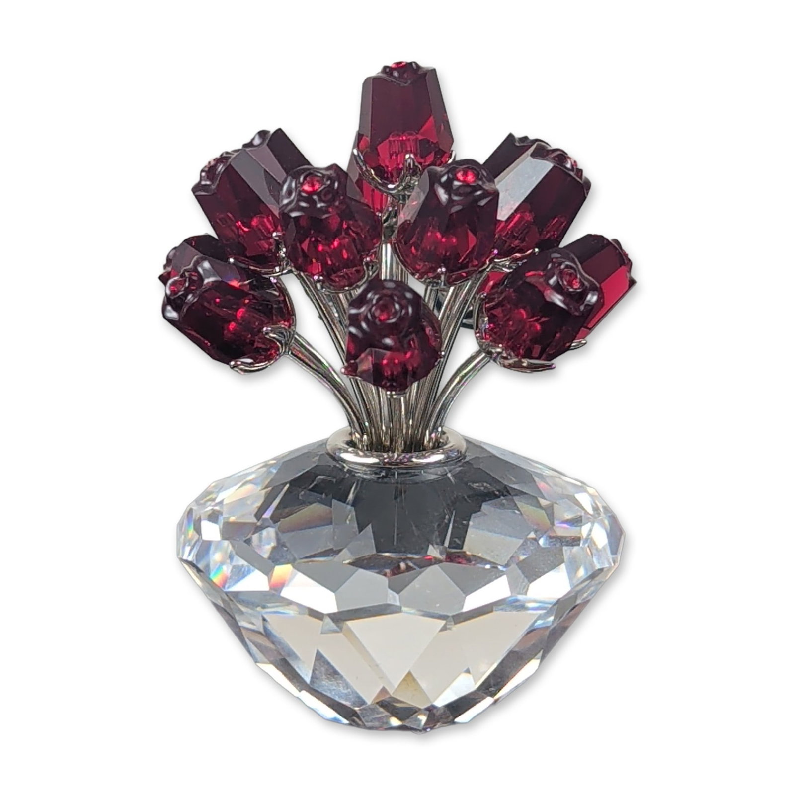 Swarovski Crystal Red Vase of Roses Figurine: Swarovski crystal figurine featuring fifteen faceted ruby red crystal rosebuds mounted on silver-tone metal stems, set within a clear faceted brilliant-cut crystal base. An etched swan logo located on