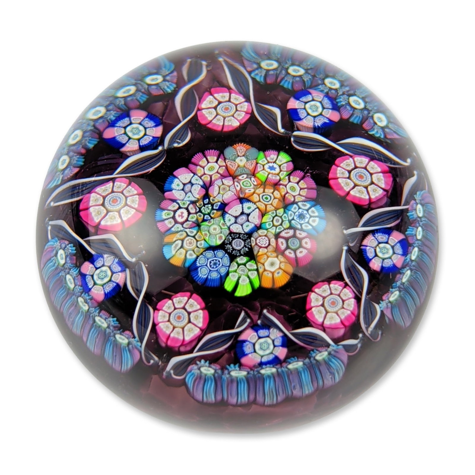 Perthshire Paperweights Concentric Millefiori Glass Paperweight: Perthshire Paperweights, Crieff, Scotland. Glass paperweight in a dome form featuring a concentric millefiori design over a deep amethyst textured crimp ground. The central multi-color cluster of cane