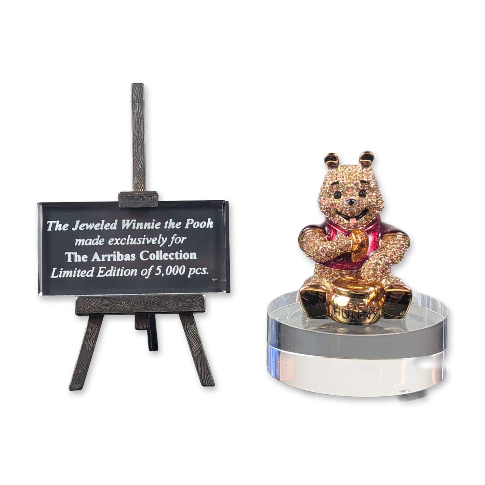 Arribas Brothers Disney Jeweled Winnie the Pooh Figurine with Stand and Base: Arribas Brothers for Disney jeweled figurine depicting Winnie the Pooh in a seated pose. The figure is constructed of gold-toned metal and is encrusted with yellow, gold, and red faceted crystals, fea