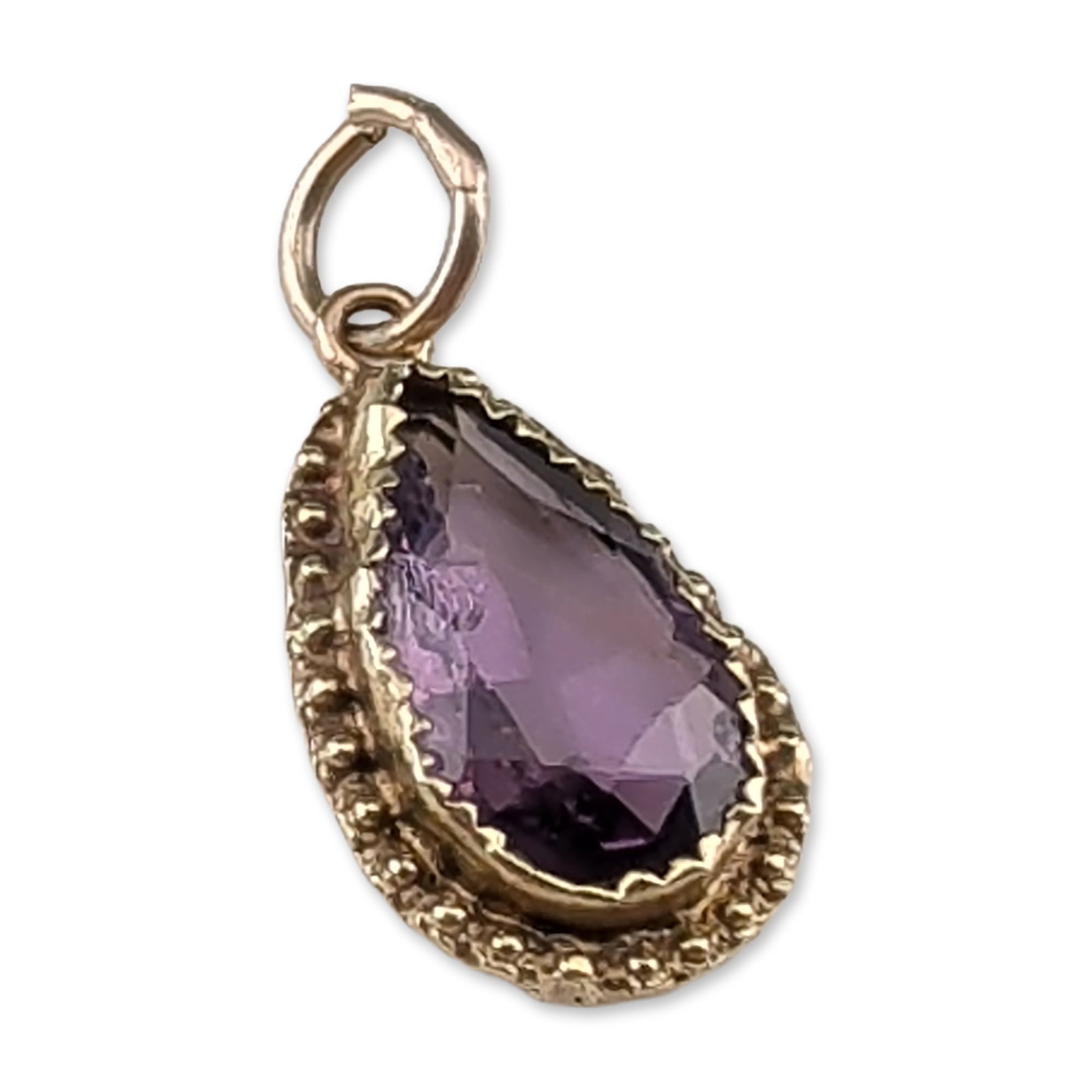 14K Yellow Gold and Amethyst Teardrop Pendant: Teardrop-shaped pendant in 14k gold featuring a pear-cut faceted amethyst. The gemstone is bezel-set within a decorative frame characterized by a scalloped and granulated border. The reverse of the pe