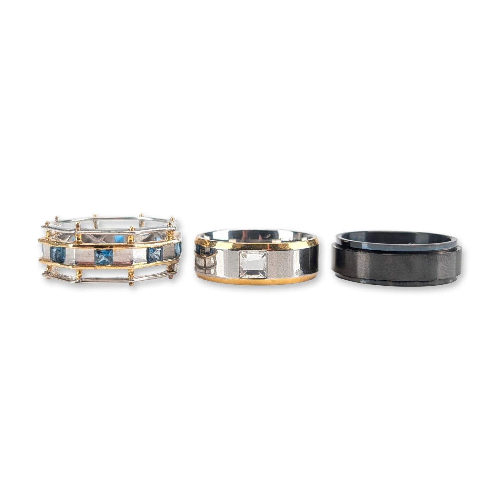 3pc Steeltime Stainless Steel Contemporary Fashion Band Rings: Three contemporary fashion band rings in various styles. The lot includes a silver architectural ring with yellow gold accents, featuring a central channel-set row of square-cut blue stones within an 