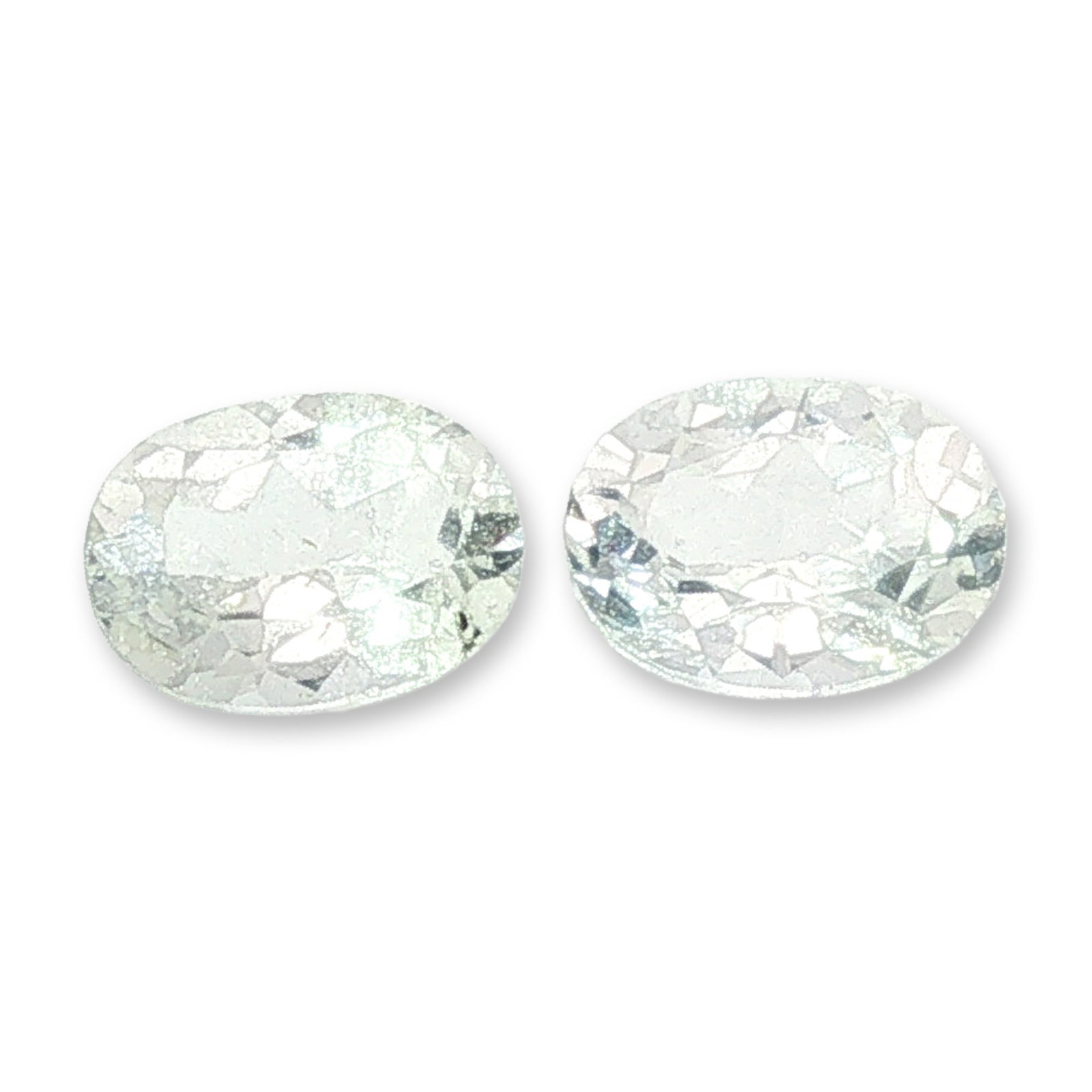 Pair of Oval Cut Colorless Topaz Gemstones: A matched pair of loose, faceted gemstones which appear to be colorless topaz. Each stone features a classic oval cut with brilliant-style crown and pavilion faceting. The pair is transparent and colo