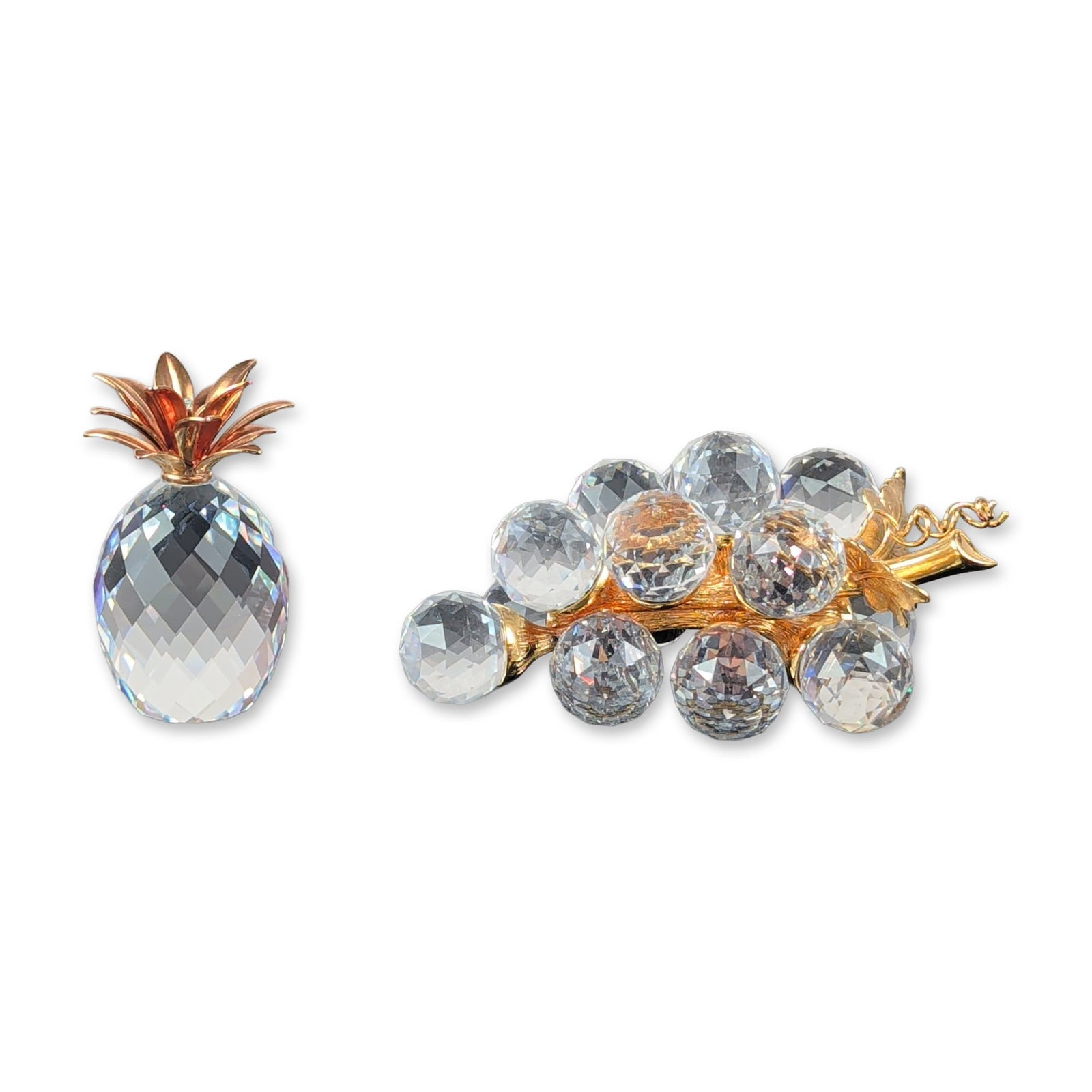 2pc Swarovski Silver Crystal Fruit Figurines Group: Swarovski Silver Crystal fruit figurines, featuring a bunch of grapes and a pineapple. The bunch of grapes figurine is constructed with faceted clear crystal spheres mounted to a textured gold-tone me