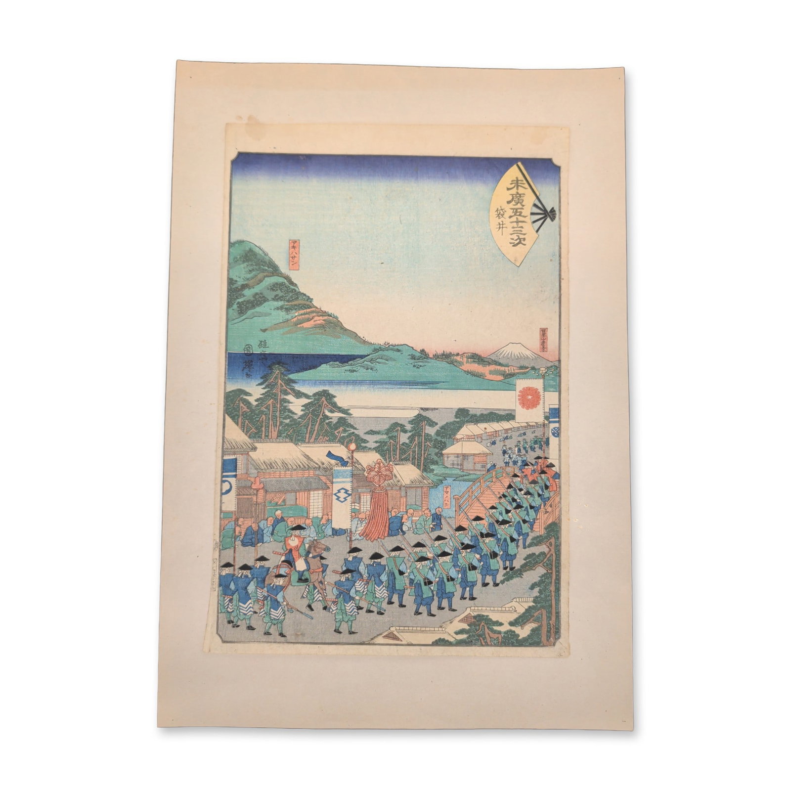 Utagawa Hiroshige II (Japanese 1826-1869) Woodcut on Paper from the Fifty-Three Stations of the: This 19th-century Japanese woodblock print features a vertical format landscape composition depicting a traditional feudal lord's procession traveling through a coastal town setting filled with local 