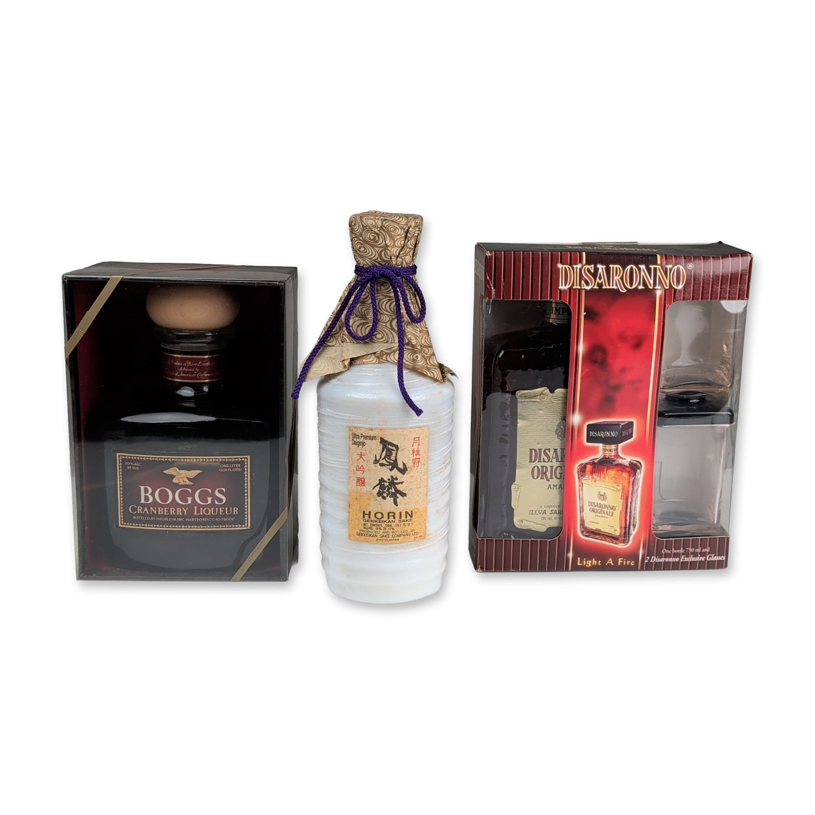 3pc Assorted Liquors - Boggs Liqueur, Gekkeikan Sake, and Disaronno Gift Set: A trio of spirit and sake items featuring two liqueurs and one sake. The collection includes a one-liter bottle of Boggs Cranberry Liqueur, bottled by Heublein, Inc. of Hartford, Connecticut, and pres