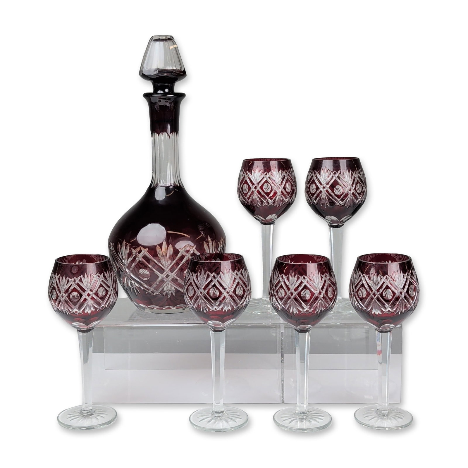 7pc Decanter Set of Bohemian Cranberry Cut to Clear Glass: Bohemian cased and cut-to-clear crystal decanter set in deep cranberry red. The set features a decanter with a matching faceted stopper and 6 wine glasses decorated with cross-hatched diamonds,