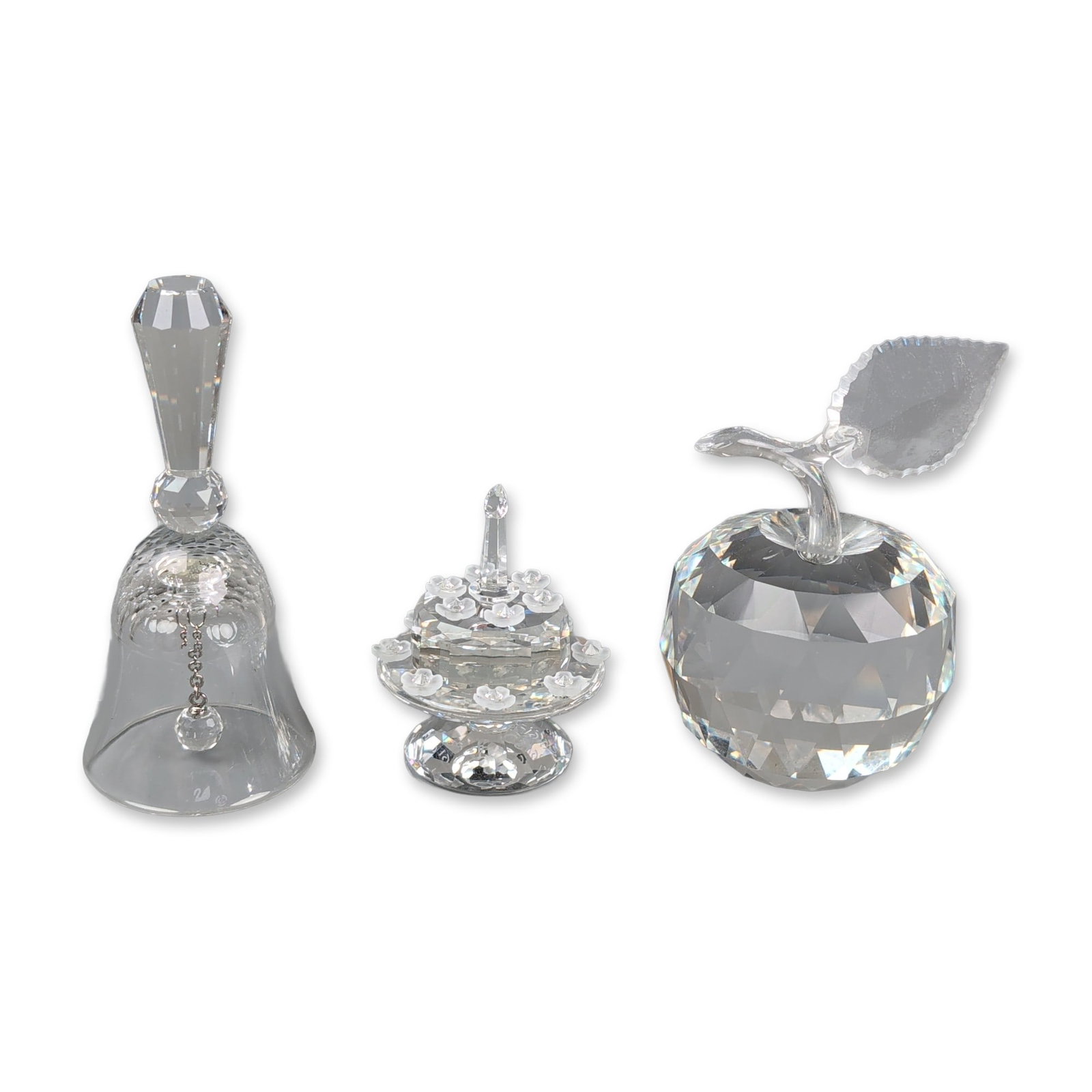 Three Swarovski Crystal Figurines, Apple, Table Bell, and SCS Birthday Cake: The three-tiered commemorative cake is decorated with frosted flowers and a candle, presented in a white anniversary box printed with 1987 - 1992 and a swan logo. The faceted apple features a clear st