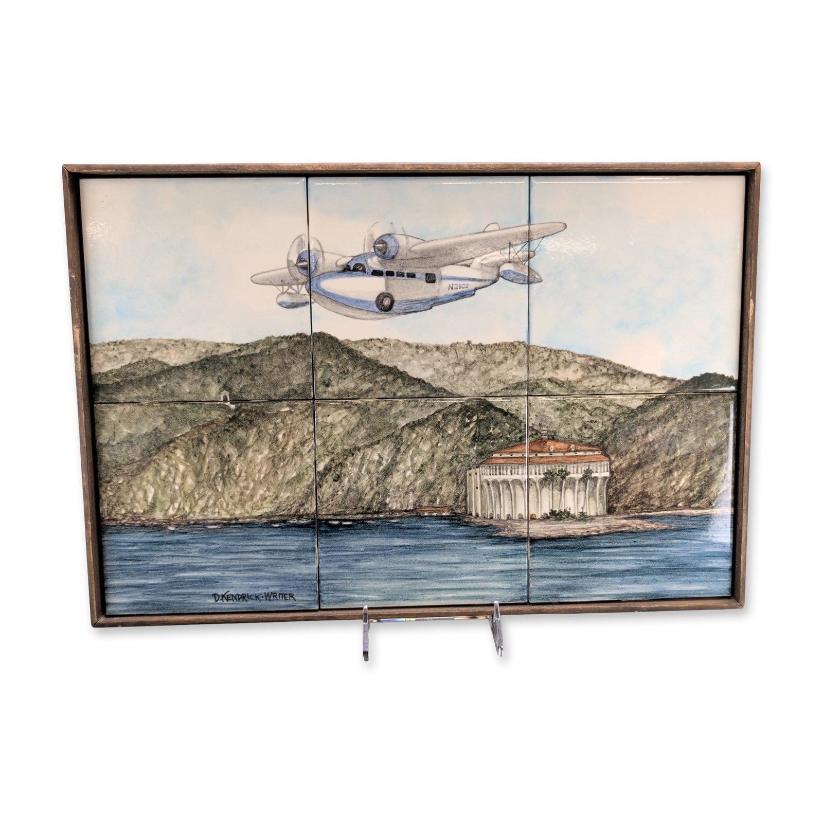 D. Kendrick-Writer 'Grumman Goose Over Catalina, Signed: A ceramic tile mural by D. Kendrick-Writer comprising six glazed tiles, depicting a Grumman G-21A Goose aircraft bearing the tail number N21CS flying over the coastline of Santa Catalina Island with t