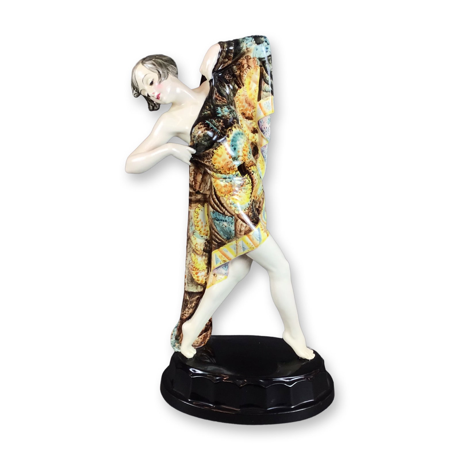 Keramos Austria Sculpture Woman Dancer: This Art Deco glazed porcelain figurine depicts a dancer. The figure is captured in a dynamic pose, partially draped in a large, vibrantly patterned robe featuring intricate motifs in shades of yellow