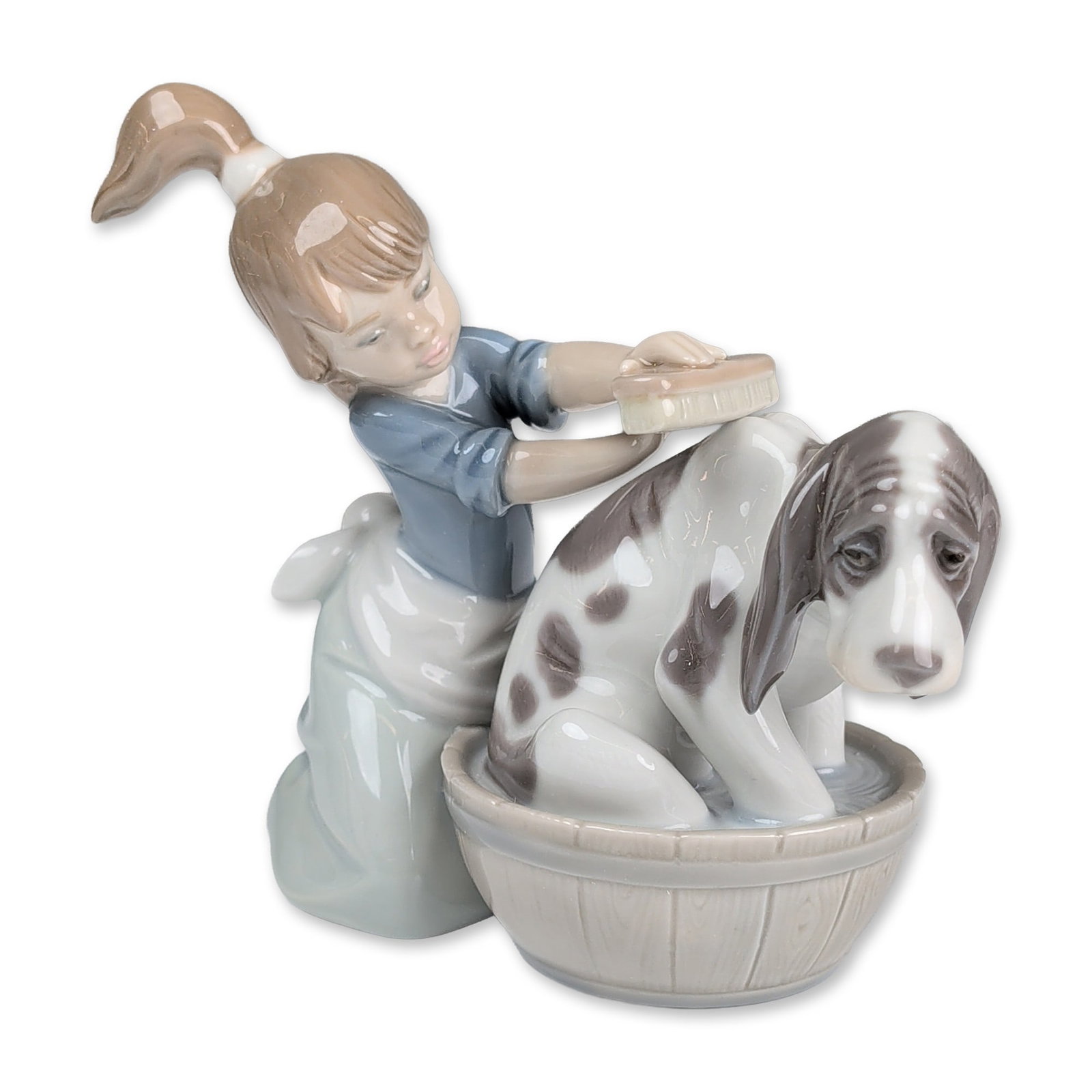 Lladro Glazed Porcelain Figurine, Bashful Bather 01005455: The piece features a young girl with a brown ponytail in a blue top and pale blue skirt washing a spotted dog in a bucket textured to resemble wood staves. The underside of the bucket features a print