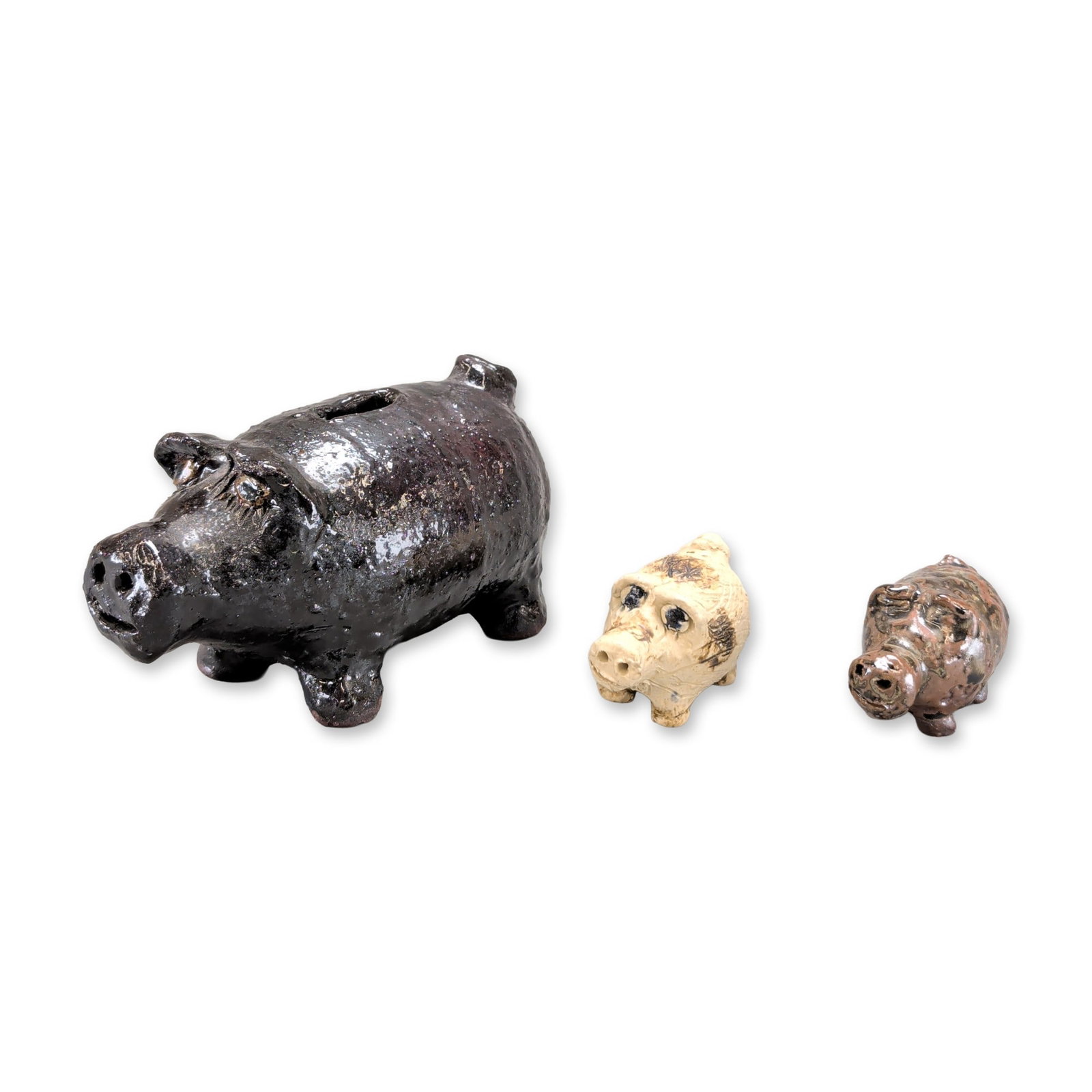 3pc Marie Rogers Pottery Piggy Bank and Figurines: Trio of hand-crafted ceramic pig figurines in graduated sizes, each featuring unique glaze treatments and modeled details. The largest figurine is finished in a high-gloss dark brown glaze and
